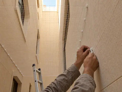 Hands fixing bird netting with clips across an open air shaft